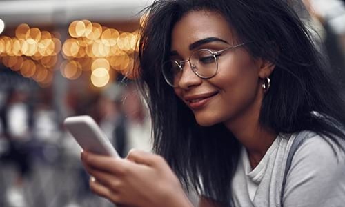 A woman happily reading on her mobile phone while enjoying the urban scenery.