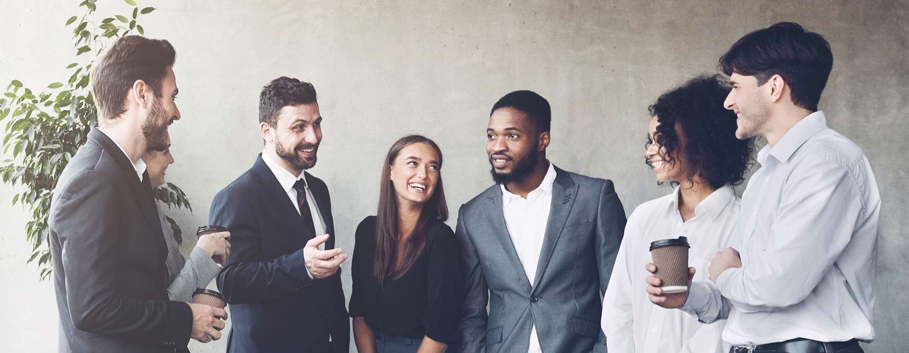 Colleagues standing and smiling at each other with a neutral grey wall in the background